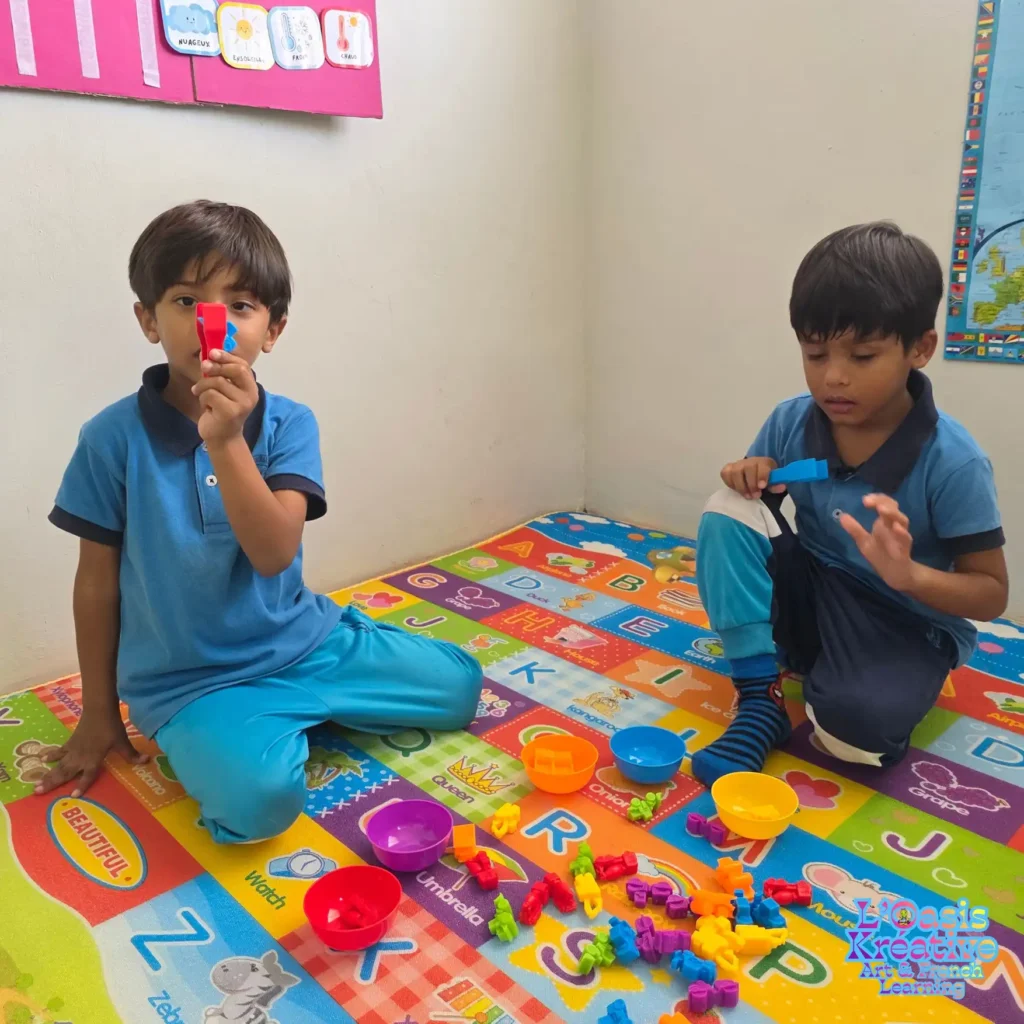 Deux jeunes enfants assis sur un tapis alphabet coloré manipulent des figurines et des bols pour un cours d'éveil au français à l'Oasis Kréative, Maurice.