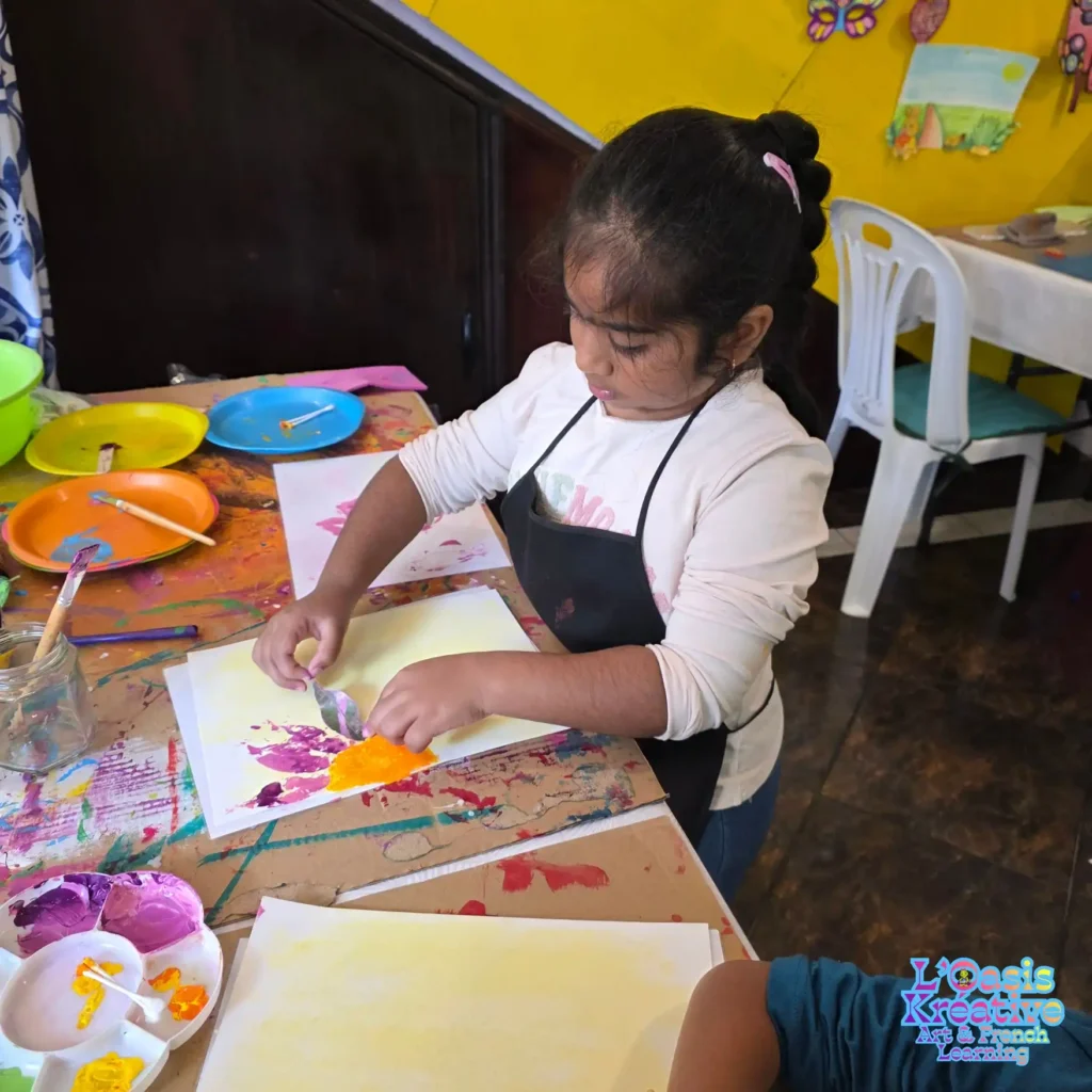 Une enfant applique délicatement une feuille peinte sur son dessin pour créer une empreinte lors d'un atelier d'impressions végétales à L'Oasis Kréative, Curepipe.