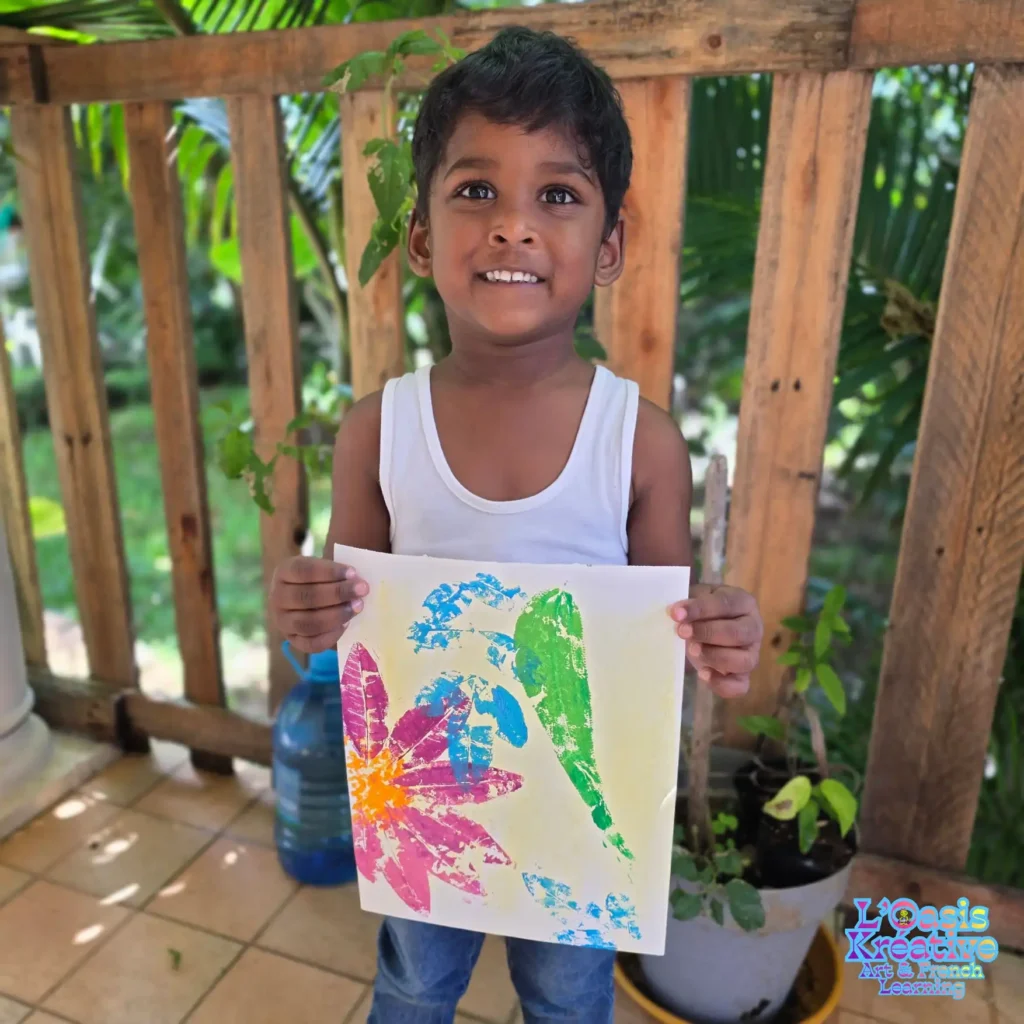 Un jeune garçon rayonnant montre son œuvre d'art faite d'empreintes de feuilles et de fleurs colorées pendant un atelier d'expression artistique à Curepipe.