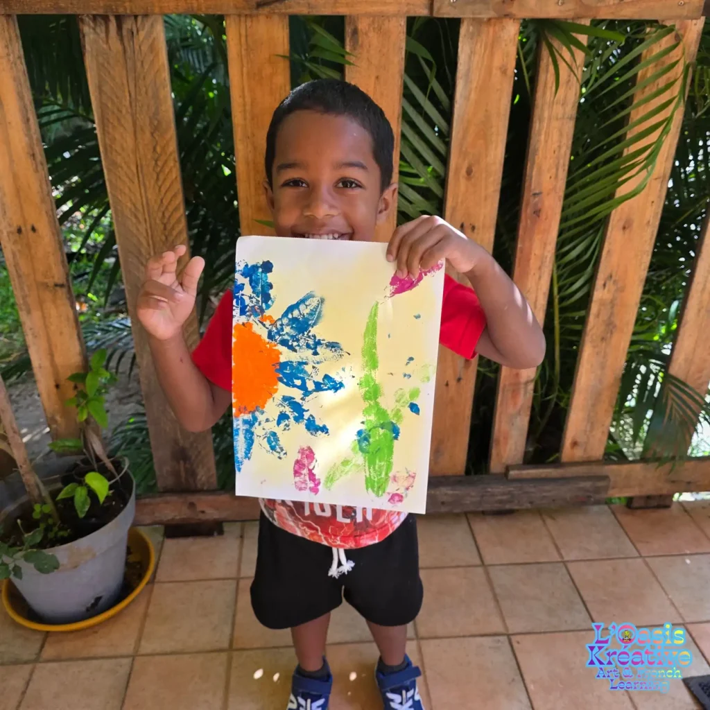 Garçon souriant tenant un tableau réalisé en impressions végétales lors d’un atelier avec Zazie Jam à l’Oasis Kréative à Curepipe.