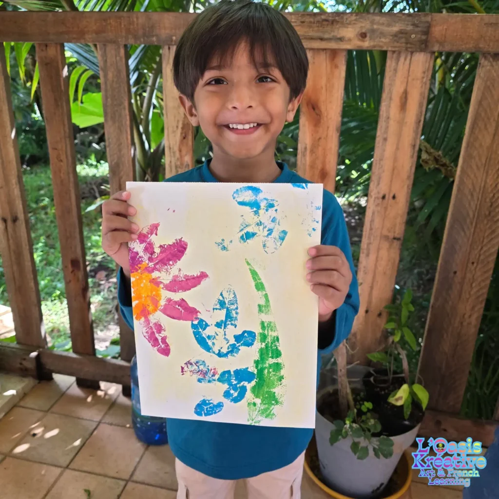 Un jeune garçon souriant présente sa peinture réalisée avec des impressions de feuilles et de fleurs colorées lors d'un atelier créatif à Curepipe.