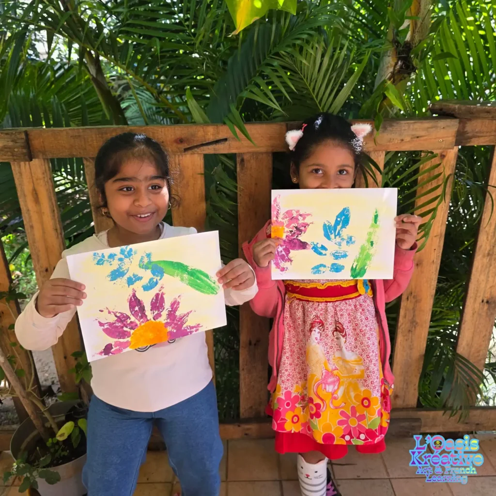 Deux petites filles souriantes montrant leurs créations en impressions végétales à L'Oasis Kréative avec Zazie Jam à Curepipe.