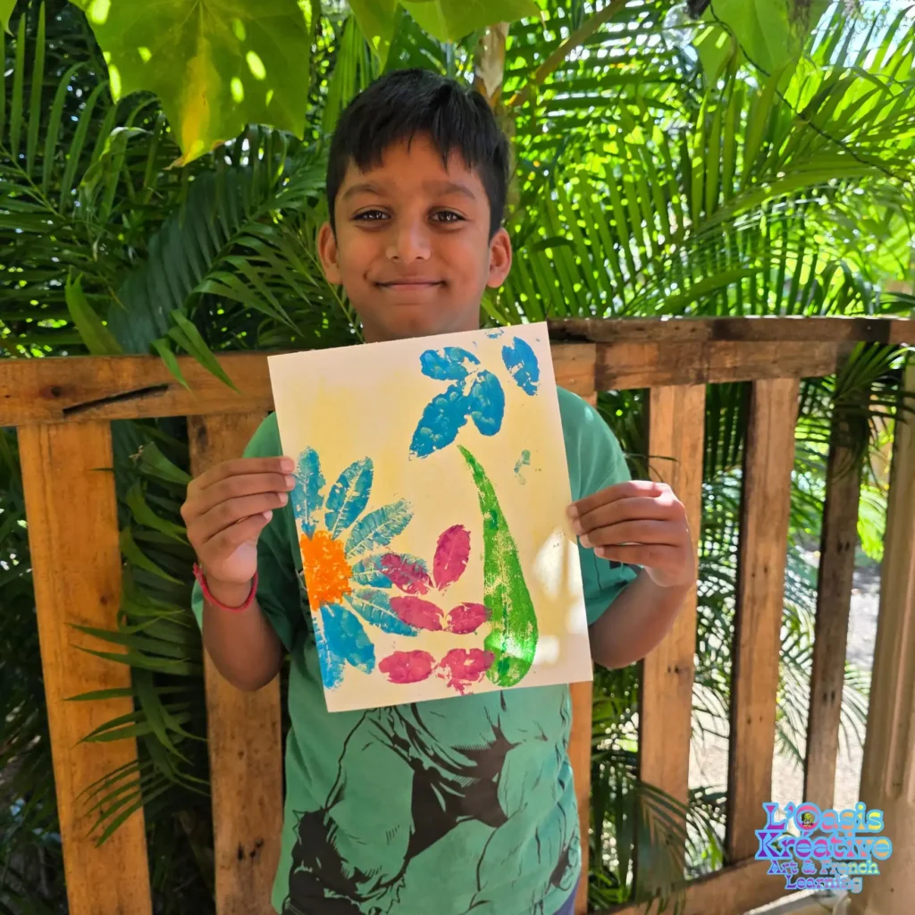 Enfant présentant un tableau coloré réalisé en impressions végétales avec des feuilles et de la peinture lors d’un atelier créatif avec Zazie Jam à L’Oasis Kréative – Art & French Learning à Curepipe.